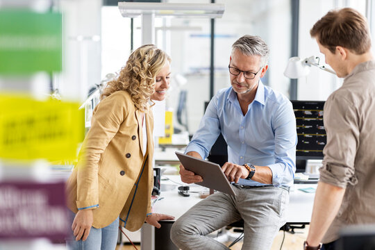 Mature businessman discussing over digital tablet with colleagues in office
