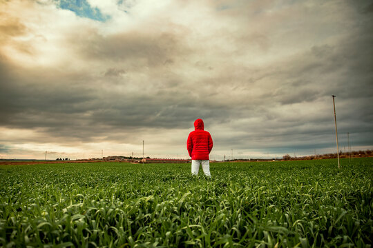 Young man with winter coat standing in field against cloudy sky during sunset