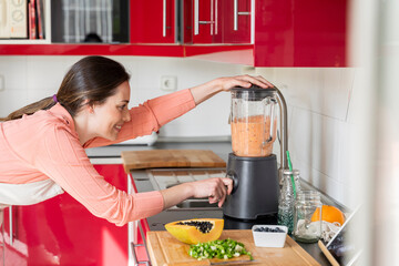 Woman using blender to prepare smoothie in kitchen at home
