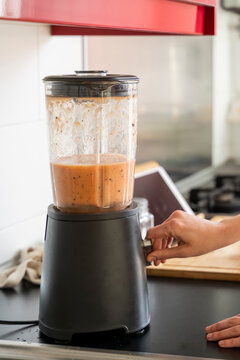 Young woman making smoothie through blender in kitchen at home