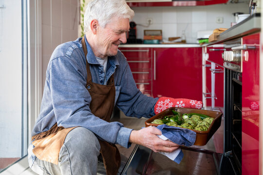 Smiling senior man putting vegetable tray in oven