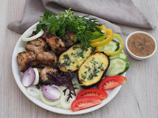 Shish kebab with herbs, fried stuffed potatoes in the skin, various fresh vegetables in a white plate on the table, top view. Delicious rustic food with grilled meat barbecue and natural vegetables