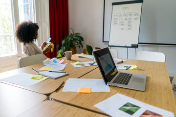 Young female entrepreneur having banana while using smart phone during coffee break in office