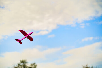 A pink plastic children's airplane toy flying in blue sky surrounded with white clouds
