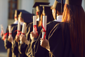 Selective focus on diverse graduation student in academic cap and gown hold diploma in commencement...