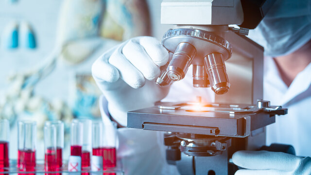 Biological scientist wear medical protective face mask looking at blood samples by using microscope doing research for new vaccine in pharmaceutical labolatory.16:9 style