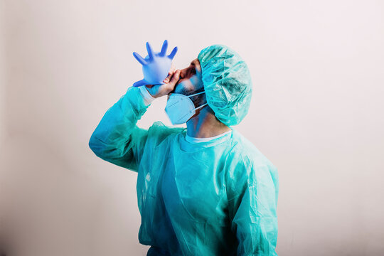 Male doctor wearing protective suit blowing surgical glove while standing against gray background