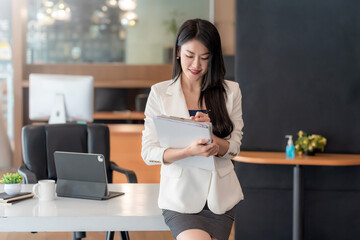 Charming businesswoman standing at the office taking notes on documents.