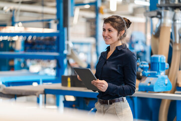 Smiling businesswoman using digital tablet while standing at industry