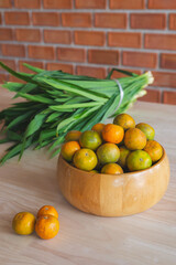 Fresh orange in the wooden bowl put on the wooden table with the pandanus behind. Orange is a healthy fruit and have refreshing sweet taste.