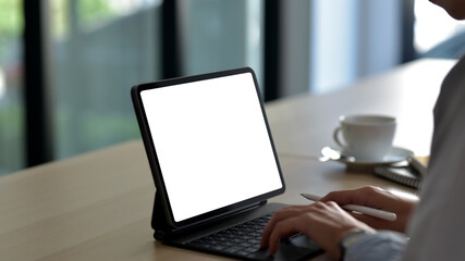 Close-up of a businesswoman holding a pen working on a tablet blank white screen at the office. Mock up.