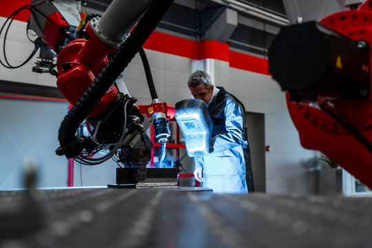 Welder with welding helmet examining robotics in factory