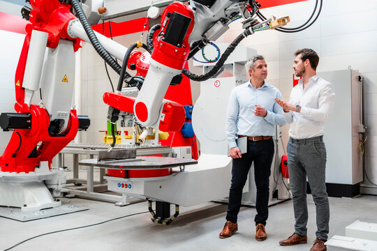 Male engineers discussing about plans by robotics in factory
