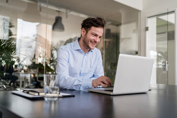 Smiling businessman using laptop at desk in office