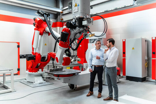 Male automation engineers discussing by machinery in factory