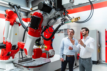 Male engineers discussing over robotic machinery in factory