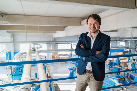 Young businessman with arms crossed smiling while standing at industry