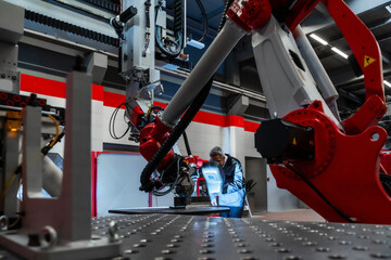 Mature worker with welding helmet working at robotics in factory