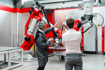 Mature engineer in jacket explaining robotics to young man in industry