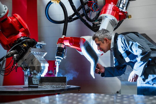 Mature worker with welding helmet working at robotics in factory