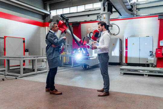 Male engineers discussing while robotics welding in factory