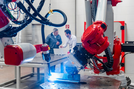 Robotic arm welding while male engineers discussing in factory