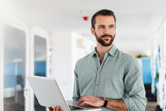 Young male professional with laptop standing at office