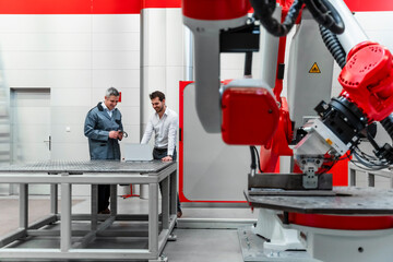 Young male entrepreneur using laptop while discussing with mature worker in factory