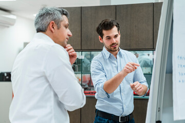 Young male entrepreneur discussing plans with colleague at whiteboard