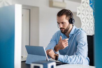 Young professional with headphones talking on video call over digital tablet at office