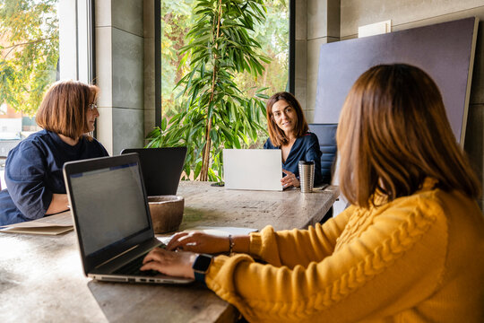 Mature businesswoman with female colleagues discussing while sitting at conference table in office