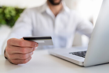 Entrepreneur with laptop holding credit card while sitting at desk in office
