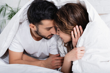 interracial couple with closed eyes lying under blanket.