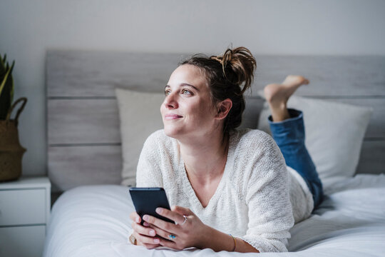 Smiling woman using mobile phone while lying on bed