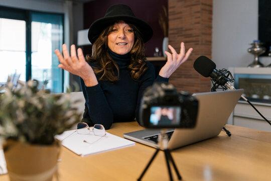 Female influencer with microphone and laptop talking while filming through camera at home