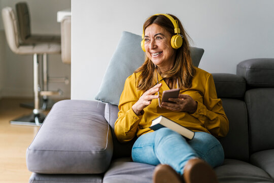 Smiling mature woman looking away while listening music through headphones at home