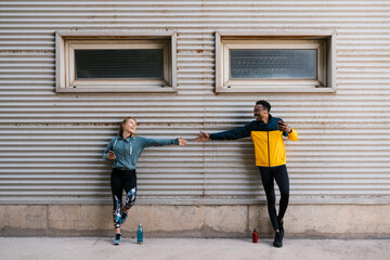 Smiling male and female athlete holding mobile phone while shaking hands against wall