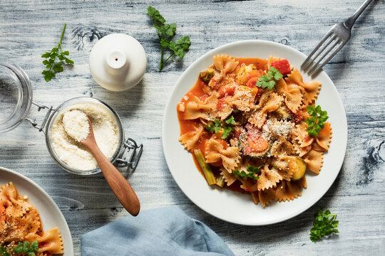 Two plates of bow tie pasta with vegetables and vegan Parmesan