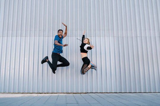 Carefree male and female friends jumping high by wall