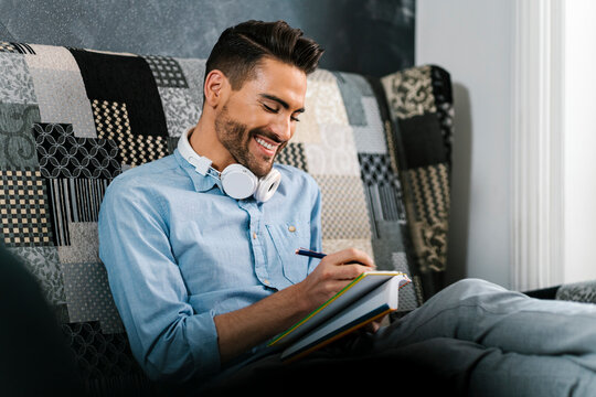 Mid adult man smiling while writing in book sitting at home