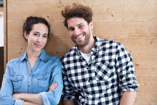 Smiling male and female entrepreneurs against wooden wall