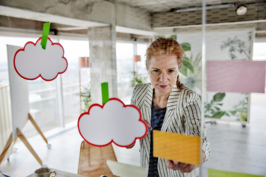 Female entrepreneur seen through glass while sticking adhesive notes on wall at office