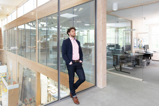 Young businessman relaxing while leaning on glass wall in factory