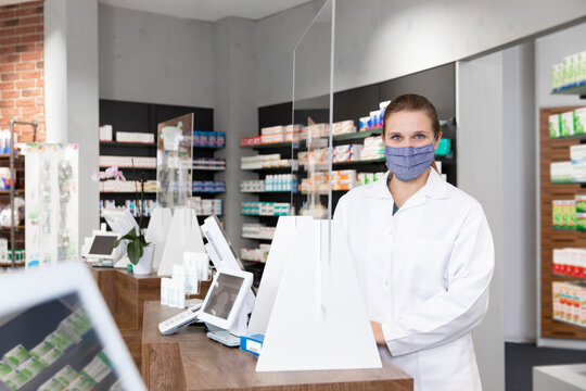 Female pharmacist in protective face mask standing at checkout in store
