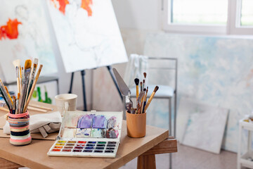 Artist's canvas and variety of paintbrush on table at home studio