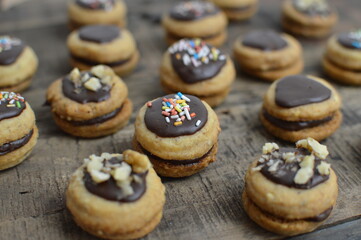 Mini traditional Austrian sandwich cookies Ischler (isleri) with chocolate and colorful sprinkles on rustic wooden table, closeup 