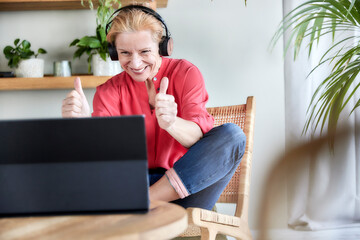 Happy mature woman showing thumbs up gesture during video call on laptop at home