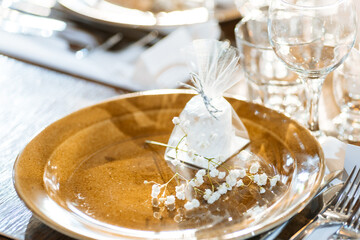 Marshmallow bonbonniere on a brown plate with a branch of gypsophila. The concept of wedding decor in the winter season. Glass goblets and table setting. Selected focus and blurred background