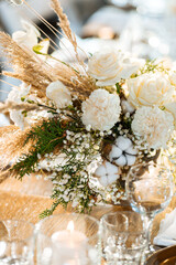 Wedding decor of roses, cotton and gypsophila and candles on a laid festive table with glasses and...