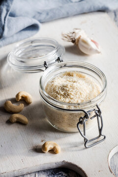 Cutting board with cashews and jar of shredded vegan Parmesan cheese